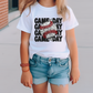 a little girl wearing a white shirt with a baseball on it