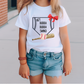 a little girl wearing a t - shirt with a baseball and bat on it
