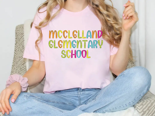 a woman sitting on a couch wearing a pink shirt that says mcclellan and elementary