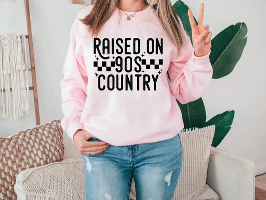 a woman wearing a pink sweatshirt that says raised on the country