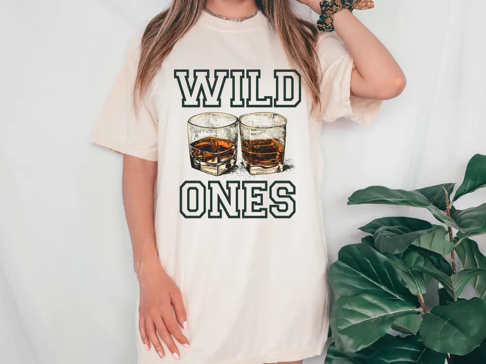 a woman wearing a t - shirt that says wild ones with two glasses of whiskey