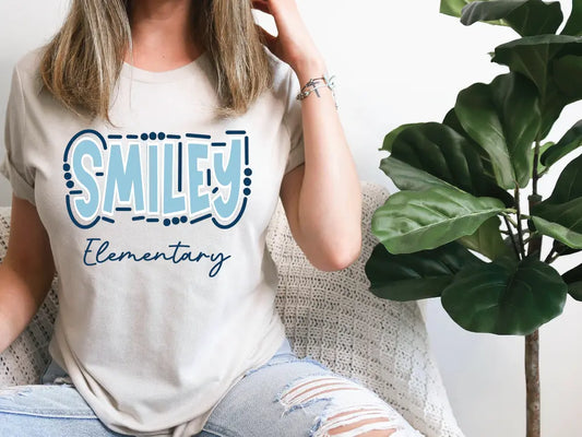 a woman sitting on a couch wearing a t - shirt that says smiley elementary