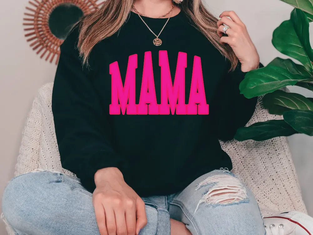 a woman sitting on a couch wearing a black sweatshirt with pink letters