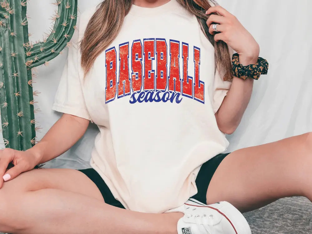 a woman sitting on the ground with a baseball season shirt on