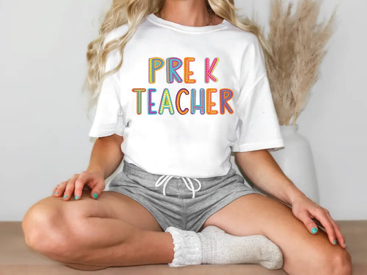 a woman sitting on a table wearing a t - shirt that says prek teacher