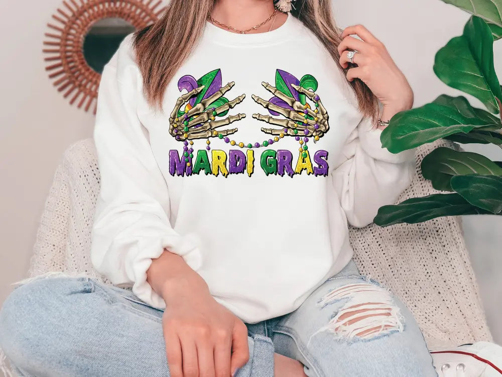 a woman sitting on a couch wearing a sweatshirt that says mardi gras